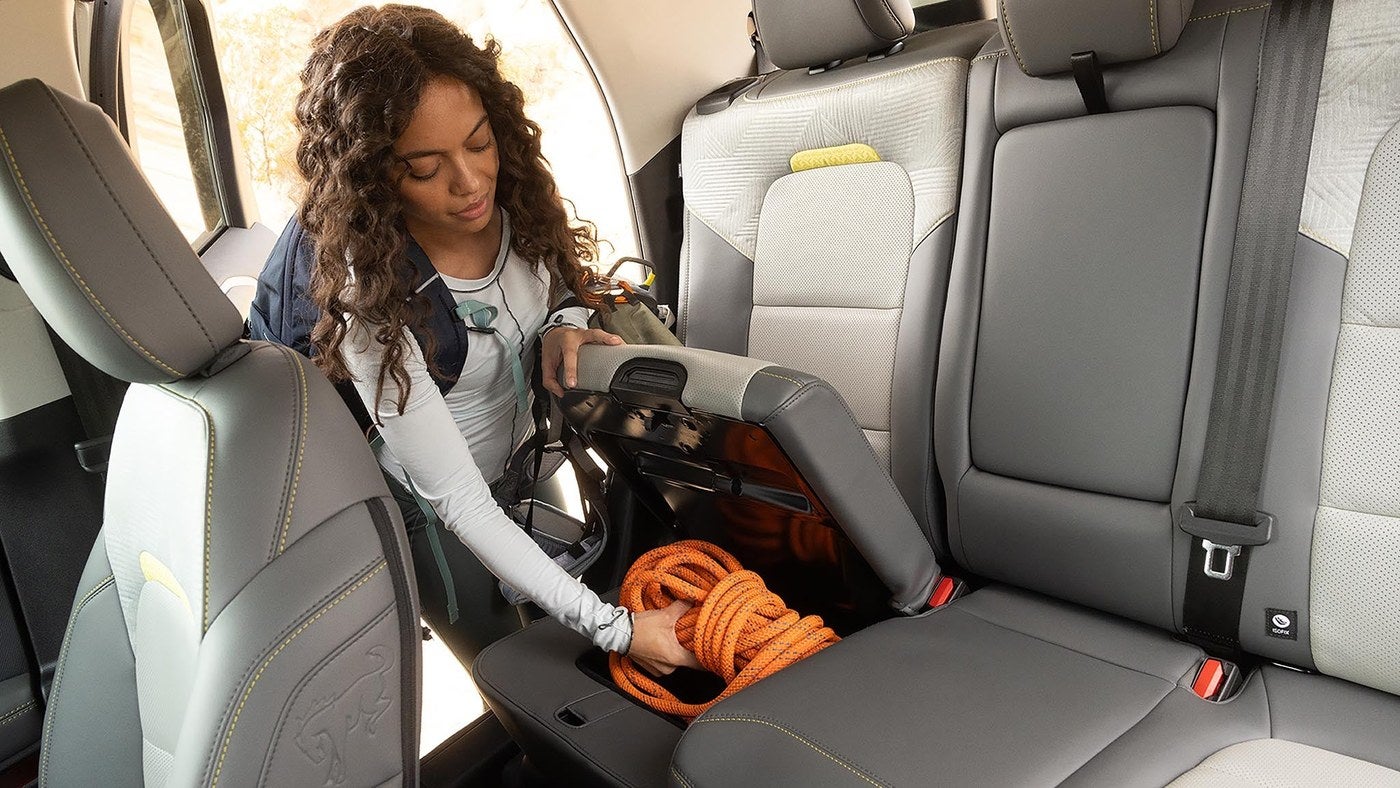 Woman handling an orange cord in the under seat storage area of the Ford Bronco Sport back seat
